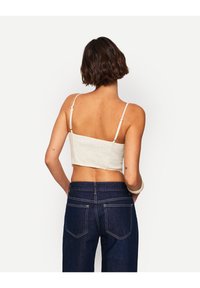 Zkrácený bílý top s tenkými ramínky, texturovaná tkanina a rovný zadní lem, spárován s tmavě modrými džíny s zadními kapsami a švy.