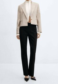 Blazer beige court avec larges revers et bouton unique, associé à un pantalon noir droit. Tissu texturé avec un design épuré.
