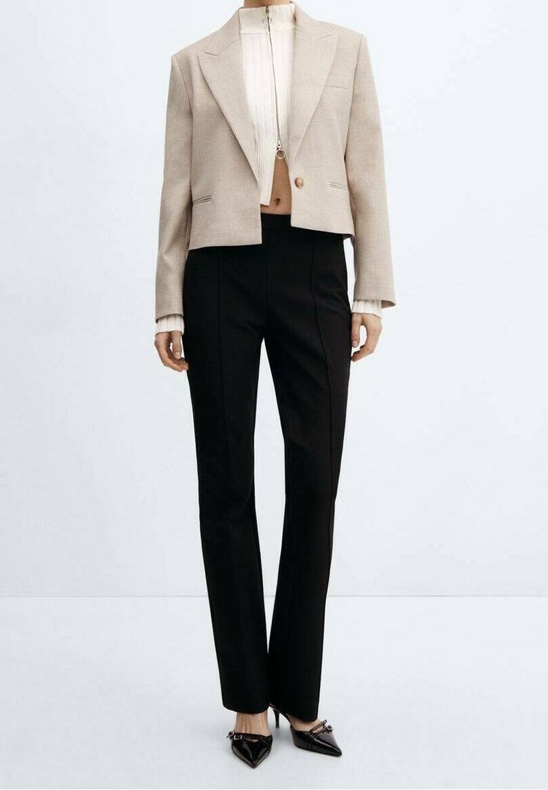 Blazer beige court avec larges revers et bouton unique, associé à un pantalon noir droit. Tissu texturé avec un design épuré.