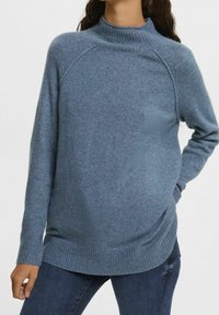 Blå stickad tröja med hög krage, ribbade mudd- och nederkanter, med en avslappnad passform och subtil struktur. Kombinerad med mörka jeans.