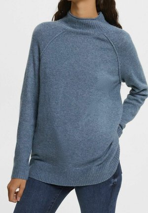 Blauwe gebreide trui met een hoge kraag, geribde manchetten en onderkant, met een ontspannen pasvorm en subtiele textuur. Gecombineerd met donkere jeans.