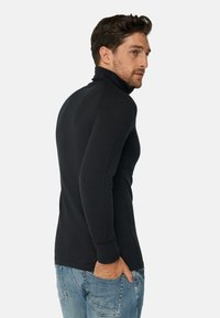 Schwarzes Langarm-Turtleneck-Oberteil mit schmaler Passform, glatter Textur und gerippten Bündchen, kombiniert mit hellblauen Jeans.