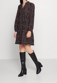 Svart mönstrad klänning med diamantmotiv, lång ärm och v-ringning. Bärs med knähöga svarta läderstövlar och en klumpig klack.