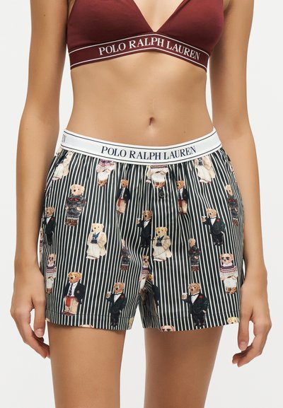 Femme portant un short boxer rayé Polo Ralph Lauren avec des imprimés d'ours en peluche et un bralette bordeaux assorti avec un bandeau à logo de la marque.
