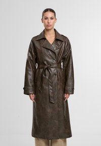 Brązowy płaszcz trench z sztucznej skóry, z paskiem w talii, podwójnymi guzikami i szerokimi klapami. Posiada kieszenie boczne oraz gładką teksturę.