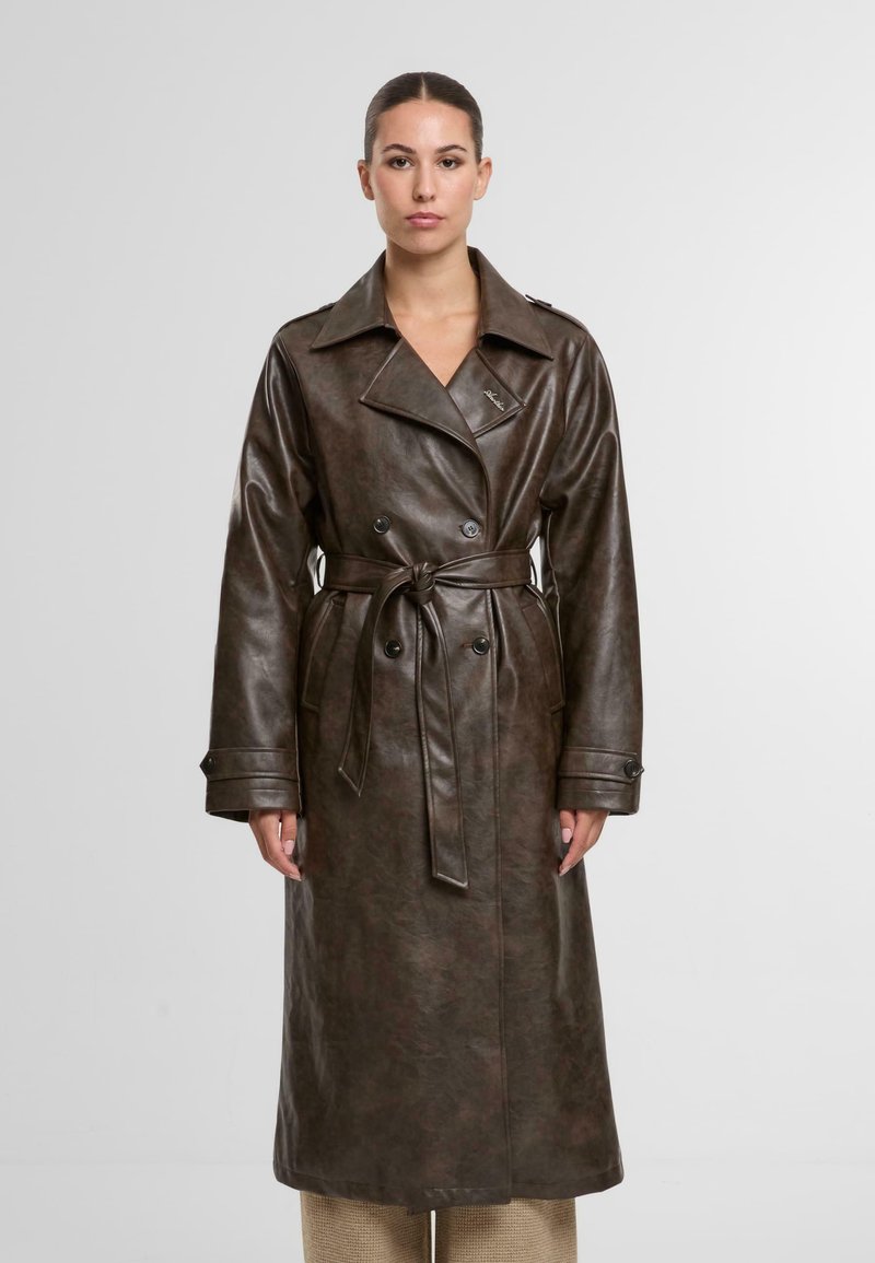 Brązowy płaszcz trench z sztucznej skóry, z paskiem w talii, podwójnymi guzikami i szerokimi klapami. Posiada kieszenie boczne oraz gładką teksturę.