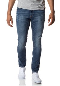 Modré džíny s úzkým střihem, s módními odstíny a pěti kapsami, nošené s bílými teniskami. Materiál působí hladkým dojmem s mírným leskem.