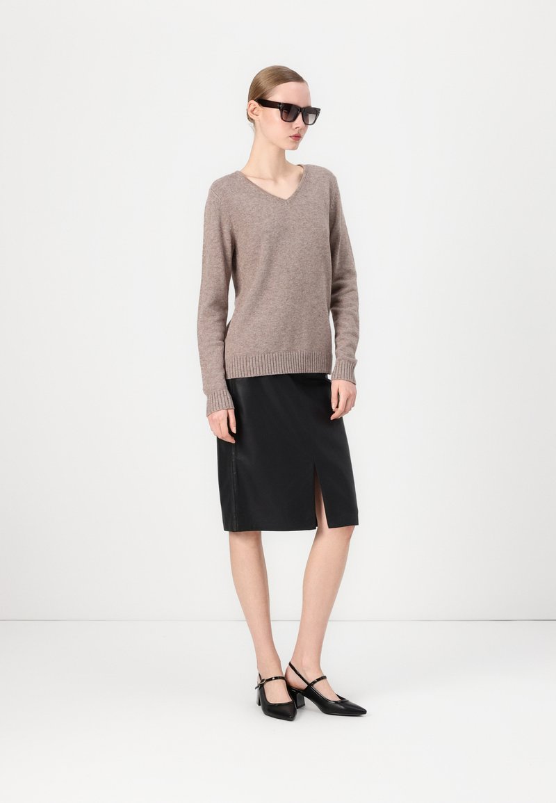 Pull en tricot marron clair avec un col en V et des poignets côtelés, associé à une jupe crayon en cuir noir avec une fente devant. Chaussures à talons slingback noires.