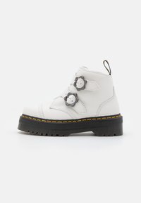 Bottes ankle blanches en cuir avec une finition texturée, dotées de deux fermetures à clip décoratives, d'une semelle noire épaisse et de coutures jaunes.