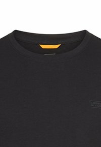 Schwarzes Baumwoll-T-Shirt mit Rundhalsausschnitt, ausgestattet mit einem kleinen gelben Etikett und einem dezenten Logo in der unteren Ecke. Glatte Textur.