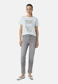 Witte t-shirt met korte mouwen en een metallic bloemenafbeelding; gecombineerd met lichtgrijze straight-leg jeans en zilveren balletschoenen.