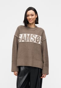 Χοντρό πλεκτό πουλόβερ σε καφέ χρώμα με αντίθετο λευκό μοτίβο "SAMSON" στο στήθος. Διαθέτει φαρδύ ριμπ τελείωμα και μανσέτες.