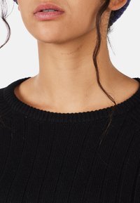 Schwarzer Rippstrickpullover mit einem weiten, runden Halsausschnitt. Nahaufnahme zeigt den strukturierten Stoff und einen subtilen Glanz.