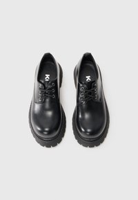 Scarpe in pelle nera con punta arrotondata, design con lacci e suole in gomma nera robuste, caratterizzate da cuciture e una finitura testurizzata.