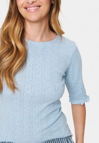 Ljusblå stickad topp med en texturerad mönster, korta ärmar med scallopkant och rund halsringning.
