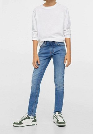 Lekka biała bluzka z długim rękawem w połączeniu z dopasowanymi niebieskimi dżinsami i sneakersami z zielonymi akcentami, prezentująca casualowy, miejski styl.