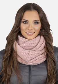 Roze gebreide infinity sjaal met een textuurpatroon, gedragen over een donkere jas. Zacht en knus uiterlijk, ontworpen voor warmte.