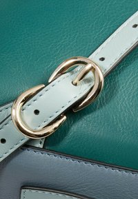 Tracolla per borsa in pelle turchese con dettagli azzurri e fibbia color oro. Presenta cuciture visibili e texture liscia.