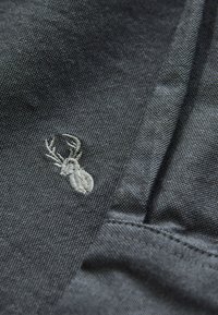 Ciemnoszara tkanina z małą, wyszywaną białą głową jelenia i porożem w pobliżu złożonego szwu.