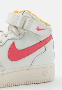 Vita läder hög-top sneakers med en rosa swoosh, beige sula och gul mesh-foder, samt ett kardborreband. Luftdämpning vid hälen.