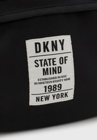 Svart tygmärke med fet svart text på vit bakgrund, som säger "DKNY STATE OF MIND," med ytterligare text och ett datum.