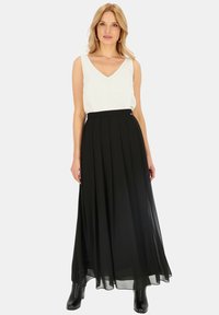 Czarna plisowana długa spódnica o zwiewnym fasonie, zestawiona z białym topem bez rękawów. Spódnica ma gładki, lekki materiał i wyraźną talię.