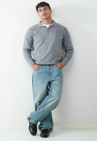 Grauer gestrickter Pullover mit Kragen, kombiniert mit hellblauen weit geschnittenen Jeans und schwarzen Schuhen. Schlichtes Design und lässige Passform.