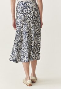Jupe évasée bleu marine avec un motif de feuilles blanches. Fabriquée en tissu léger, elle présente une texture lisse et une longueur mi-mollet.