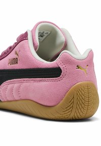 Rosa Wildlederschuh mit schwarzen Lederakzenten, goldenem Puma-Logo, weißem Kragen und strukturierten gummiartigem Sohlenprofil mit gewölbtem Profil.