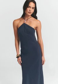 Navy-Kleid mit Halterneck-Design, aus leichtem Stoff gefertigt, mit einer subtilen strukturierten Oberfläche und einem Anhängerakzent am Ausschnitt.
