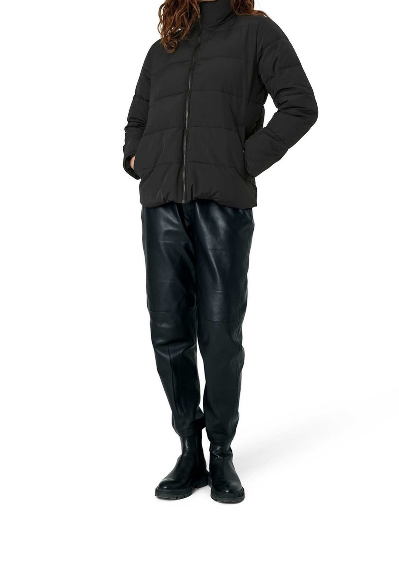 Svart puffjacka med hög krage och dragkedja, kompletterad med glänsande svarta läderbyxor och svarta ankelskor.