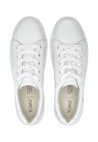 Weiße Schnürschuhe mit niedrigem Schnitt und abgerundeten Zehen sowie gepolsterten Kragen, aus der Vogelperspektive betrachtet, mit TOMS-Branding im Inneren der Schuhe.