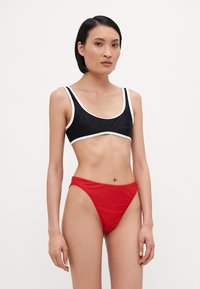 Top de bikini negru cu detalii albe și slipuri roșii cu talie înaltă. Textură netedă, design minimalist și croieli sport.