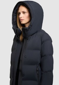Navy-blauer Puffer-Mantel mit großer, isolierter Kapuze, Reißverschluss und Druckknopfverschluss sowie verstellbaren Kordeln. Merrt einen glatten, glänzenden Finish.