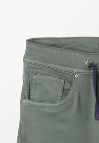 Zielone bawełniane spodnie o miękkiej fakturze, z zakrzywionym pasem, przednią kieszenią oraz granatowym sznurkiem ze srebrnymi akcentami.