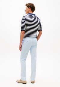 Πλεκτό πουλόβερ με ρίγες σε ναυτικό μπλε και λευκό, σε συνδυασμό με ανοιχτόχρωμο μπλε παντελόνι. Το ύφασμα φαίνεται διαπνεόμενο, με άνετη εφαρμογή και κοντά μανίκια.