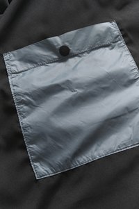 Fekete szövet hátterű, négyzet alakú, könnyű, szürke zseb fekete gombbal és varrott szegéllyel.