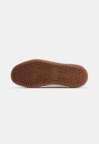 Semelle de chaussure avec motifs de bande de roulement circulaires et rayés et logo Puma embossé en caoutchouc marron sur fond clair.