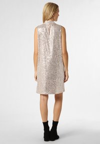 Bezramienna sukienka do kolan w jasnoróżowym kolorze z cekinowym wykończeniem, z tylnym wycięciem w kształcie dziurki i prostą sylwetką. Noszona z czarnymi botkami za kostkę.