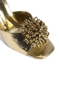 Gouden open teen hak met een gestructureerde metallic afwerking, voorzien van een grote gouden spiraaldecoratie aan de voorkant. Vierkante teenontwerp.