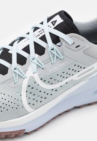 Gros plan sur une chaussure de course sur sentier Nike grise et noire avec des lacets bleu clair et un dessus en mesh ventilé.