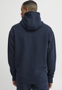 Sudadera azul marino con una gran capucha, puños y dobladillo de canalé, fabricada en tela suave. La vista trasera no muestra patrones ni acentos notables.