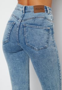 Ljusblå högmidjade jeans i denim, med en läderetikett baktill, flera fickor och en figurnära design med subtila blekningar.