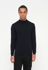 Sweter z golfem w kolorze granatowym, dziany, z długimi rękawami i ściągaczami. Materiał wydaje się miękki i teksturowany. Minimalistyczny design, bez widocznych logo.