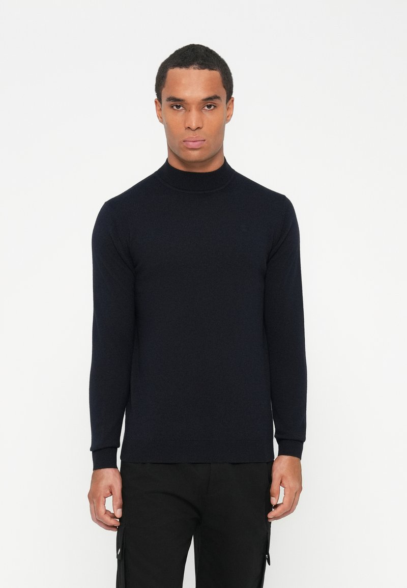 Sweter z golfem w kolorze granatowym, dziany, z długimi rękawami i ściągaczami. Materiał wydaje się miękki i teksturowany. Minimalistyczny design, bez widocznych logo.