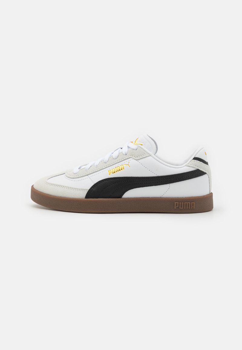 Baskets basses blanches Puma avec bande noire, semelle en gomme, lacets blancs et logos Puma dorés sur le côté, la languette et le talon.