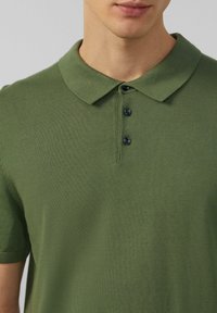Zielona koszulka polo z teksturowanej tkaniny, z klasycznym kołnierzykiem i trzema czarnymi guzikami z przodu.