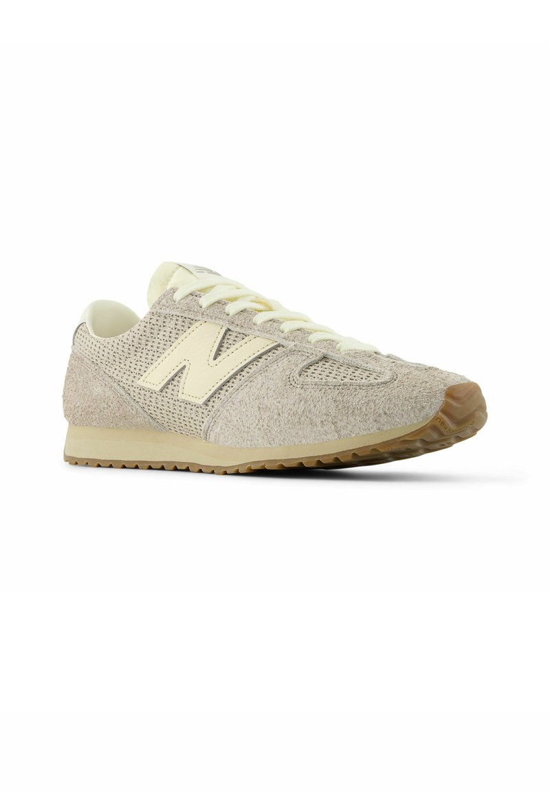 Beige sneaker with textured fabric and mesh upper, featuring a prominent cream-colored 'N' logo, white laces, and rubber outsole.