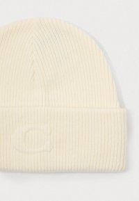 Crèmekleurige gebreide beanie met ribbeltextuur en een omgeslagen rand. Bevat een subtiele reliëfletter "C" op de rand.