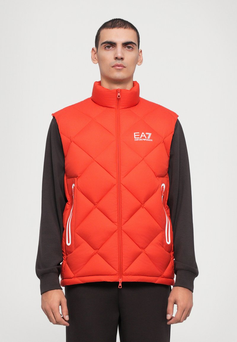 Crveni dubljeni prsluk s visokim ovratnikom, zatvaranjem na zip i bijelim detaljima. Ima bočne džepove i EA7 logo na prsima.